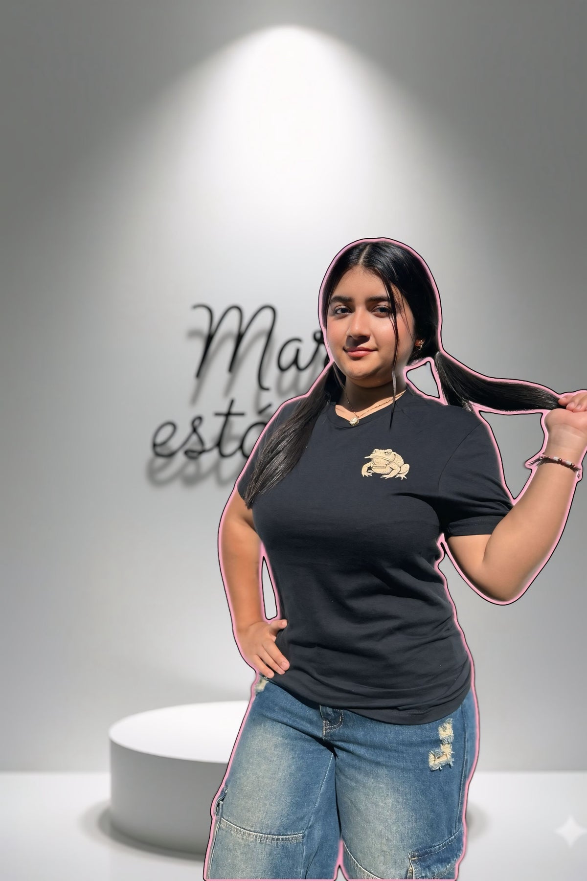 Person wearing a black t-shirt with a logo and blue jeans, standing against a gray background.