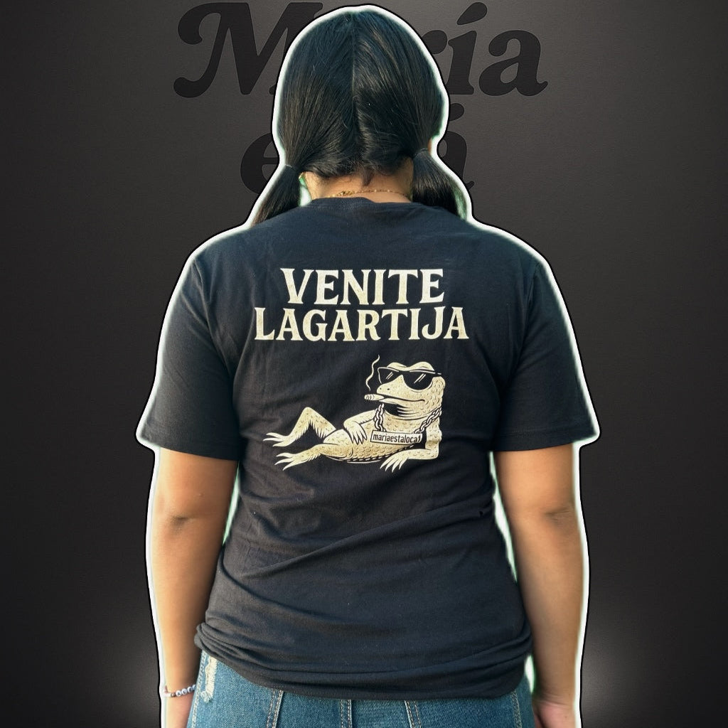 Person wearing a black t-shirt with 'Venite Lagartija' text and graphic on the back, standing against a dark background.