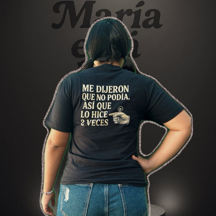 Person wearing a black t-shirt with text on the back, standing against a dark background.