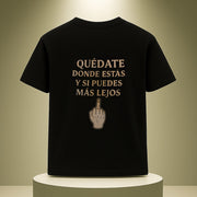 Black t-shirt with Spanish text and middle finger gesture on a white pedestal against a beige background